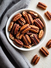 Fototapeta premium Overhead shot features pecans in white bowl on grey cloth. Nuts scattered around. Nuts look sweet, crunchy. Food performs as snack baking ingredient. Perfect for dietary recipes, display.