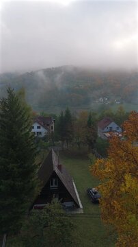 Wooden A-frame cabin surrounded by colorful autumn trees and misty mountain slopes. Vertical video	