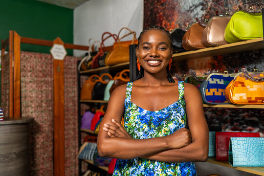 African woman small business owner smiling with arms crossed in her retail store selling handbags