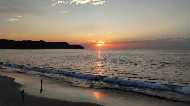 People Watching and Photographing a Dramatic Orange Sunset Over the Ocean at Cabuyal Beach, Costa Rica