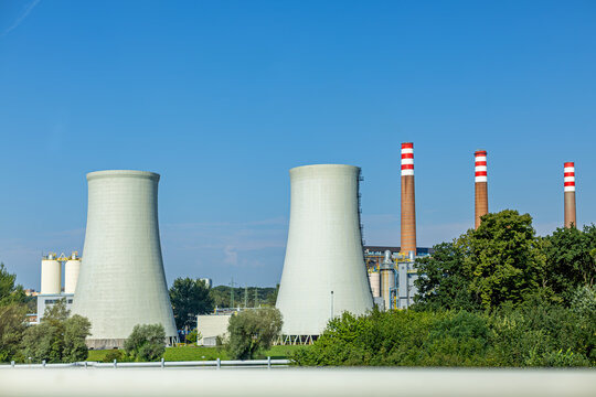 Industrial landscape with large cooling towers and chimneys of a thermal power plant under a clear blue sky. Cogeneration power facility, clean energy and electricity generation concepts.