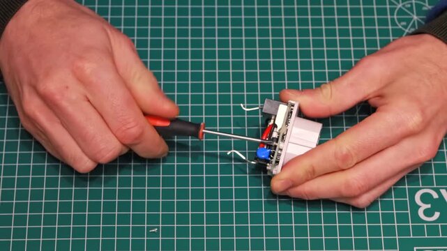 Technician Unscrewing Small Screw from Smart Plug Circuit Board with Precision Screwdriver