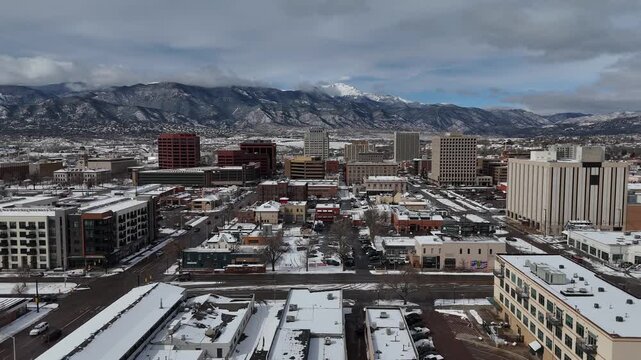 Colorado Springs downtown skyline and urban architecture set against the snow-capped Rocky Mountains under a dramatic cloudy sky 4k aerial drone video