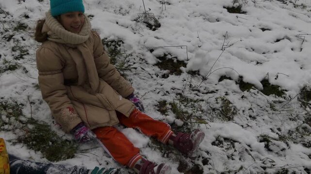 Two little girls sisters are sitting in snow in winter city park.