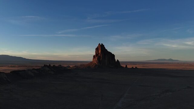 Shiprock volcanic monolith rising from the high desert plains of New Mexico during a dramatic golden hour sunset 4k aerial drone video