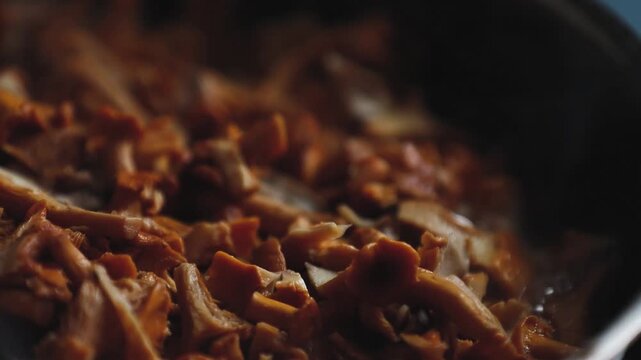 Close-up of a large pile of orange chanterelle mushrooms, showing curved caps, stems and textured gills in warm natural light.