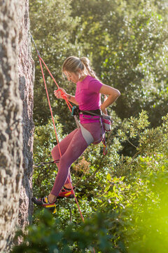 Young woman rappelling down rock cliff outdoors