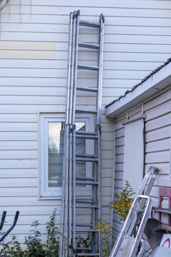 Aluminum extension ladder leaning against a house wall with white siding