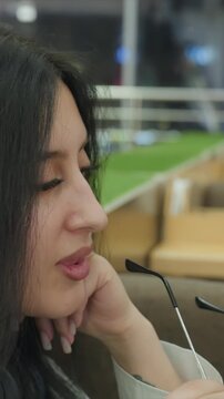 Close up of woman holding. Scene shows woman hand with long nails. Background includes blurred seating or display area suggesting public space lighting is soft and ambient