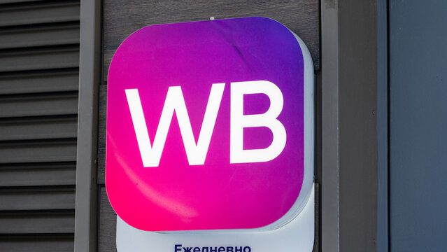 Square sign with rounded corners. Pink and purple gradient background. White 'WB' letters are bold and central. Small text appears below the logo. Mounted on a building wall, Moscow, August 10 2026.