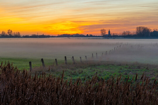 Mist in field at sunset with church tower, West Flanders, Belgium.
