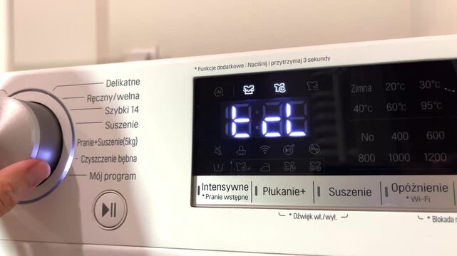 A person adjusts dial settings on a modern washing machine control panel at home, home appliance services, technology, clean home.