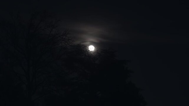 A glowing full moon in the dark and cloudy night