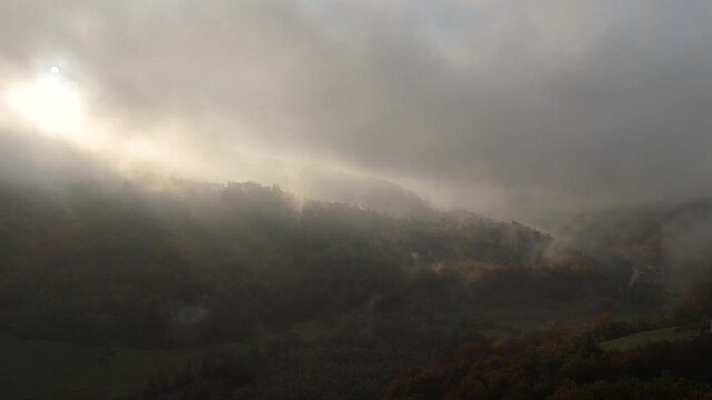 Aerial view of mountain forests shrouded in morning mist with dramatic sunbeams breaking through the clouds	