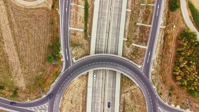 Several vehicles move on a roundabout that connects to a highway. The area has patches of grass and fields, showing clear weather and daylight.