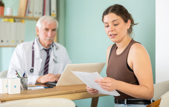 Girl patient leaves doctors office with medical counsel or guidance. Visitor examines documents, reads recommendations. After medical appointment, patient reads doctors recommendations .