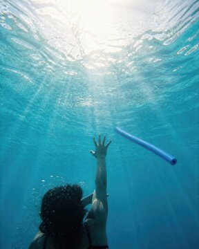 Drowning swimmer reaching for floating pool noodle underwater