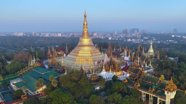 Aerial drone view at Shwedagon Pagoda, a golden stupa, surrounded by lush greenery and urban development in Yangon (Rangun), Myanmar (Burma), showcasing the city's blend of religious and modern life.