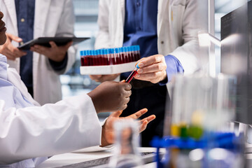 Lab researchers perform an experiment with blood samples in a tray of vials, using molecular...