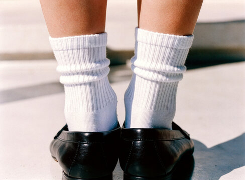 Rear view of feet standing on concrete in white crew socks and black loafers