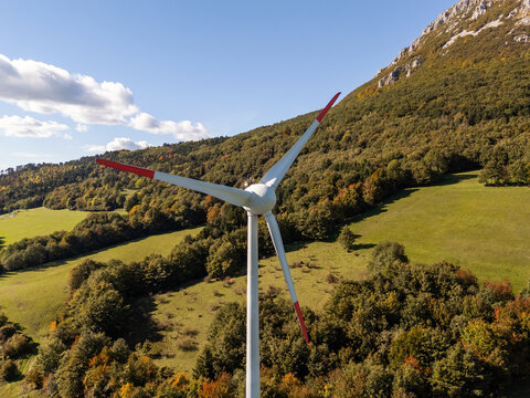 Wind turbines are producing renewable energy in a rural area surrounded by hills. The scene shows clean energy production and green fields.