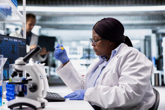 Black woman examines flasks and chemistry tools in a research lab for molecular biology study, biotechnology, medical research and healthcare technology.