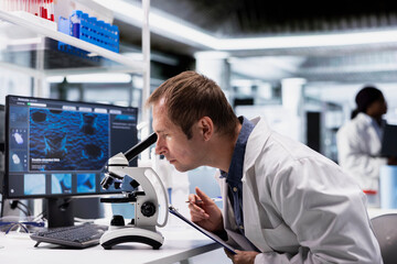 Male scientist investigates tray samples under optical microscope