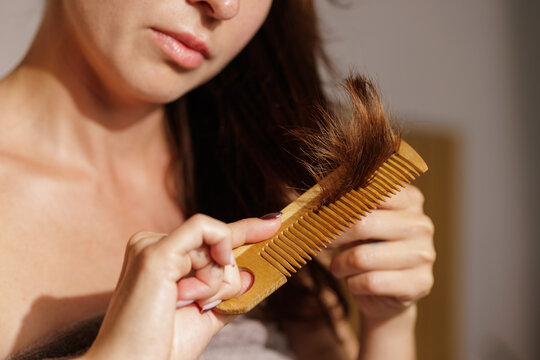 Woman examining damaged split hair ends on wooden comb