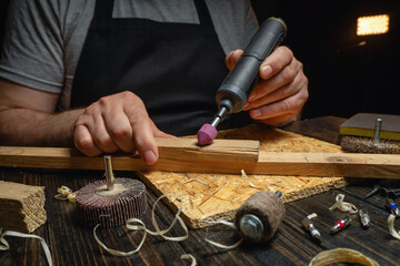 A joiner works in a workshop with a rotary tool on a piece of wood. The setting has dim lighting and various tools and materials scattered around © Віталій Б.