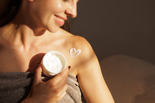 Woman Applying Moisturizing Body Cream After Shower in Warm Light