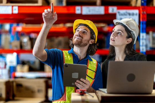 Collaborative logistics team reviewing stock availability in a large warehouse. Industrial specialist pointing at high shelves with a manager for inventory audit and strategic planning.