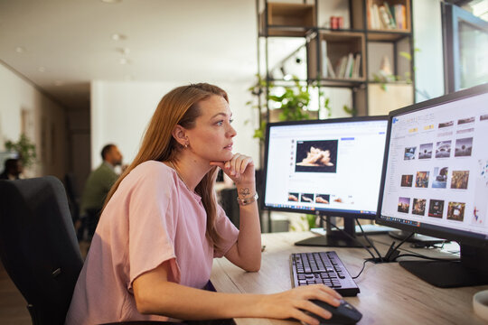 Young woman editing photos on dual monitors in modern office