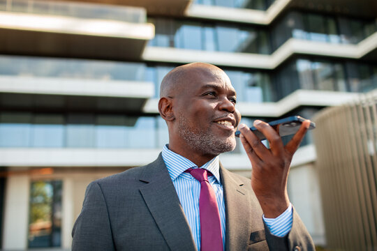 Confident businessman using voice assistant outside modern office building