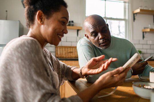 Happy couple using smartphones at home kitchen table