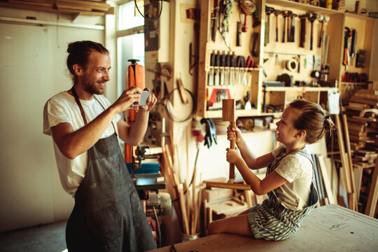 Father photographing daughter with wooden project in carpentry workshop