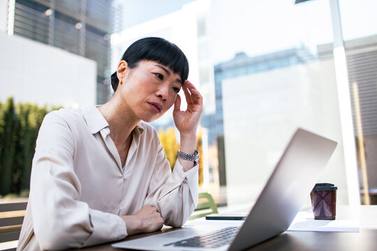 Stressed businesswoman using laptop at outdoor city cafe