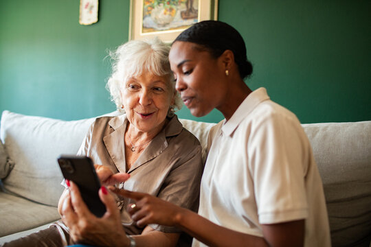 Younger woman helping senior woman use smartphone at home