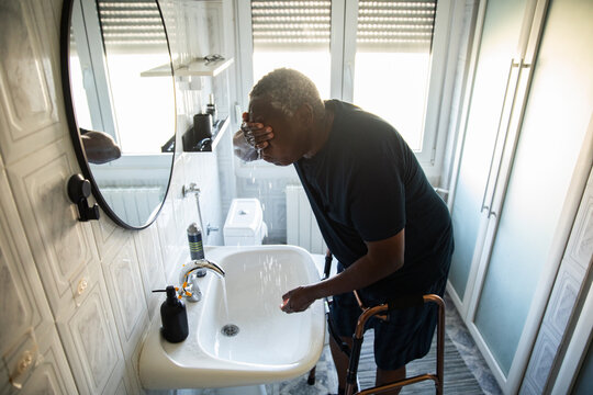 Senior man washing face with walker in home bathroom