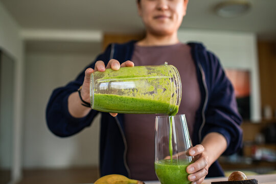 Woman pouring green smoothie in home kitchen