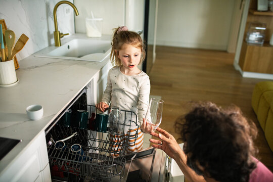 Child helping parent unload dishwasher in home kitchen