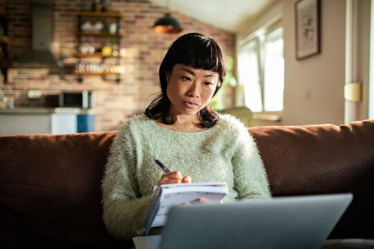 Thoughtful woman taking notes while studying at home