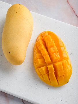 Whole and cubed mango on white speckled cutting board