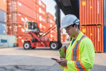 Fototapeta premium Forklift moves cargo between stacked shipping containers at a busy logistics shipping container terminal yard.