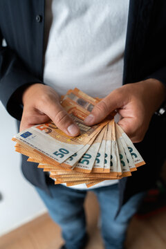 Vertical. Close-up of a person holding and counting a large stack of fifty euro banknotes indoors, representing income, savings, salary, wealth and personal financial management.