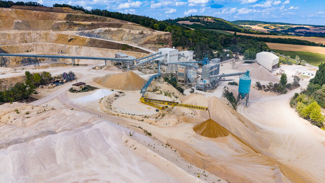 Aerial view of a sand processing facility and conveyor system. Mechanical equipment pours sand onto a tall mound inside a stone and aggregate quarry.