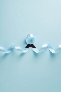 Men's health awareness blue ribbon concept with mustache on pale blue vertical background for awareness month