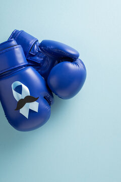 Blue boxing gloves with ribbon and mustache representing men's health and prostate awareness month on vertical pastel backdrop