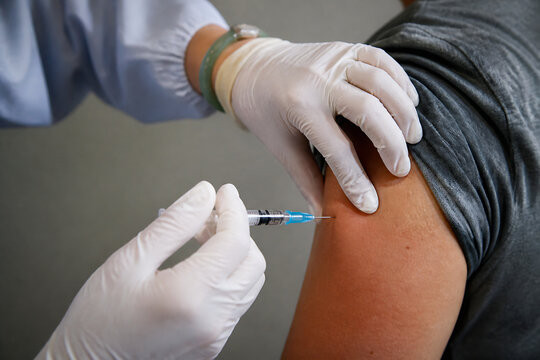 A healthcare professional in gloves is administering an injection into a person's upper arm.