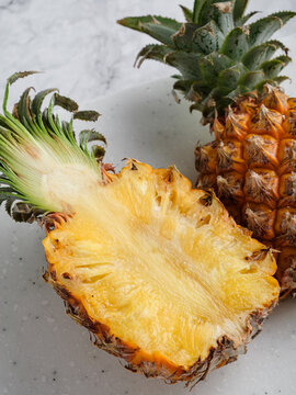 Two pineapples whole and halved on white speckled cutting board