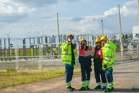 Three renewable energy engineers compare as built drawings outside the switchyard on the service road beside the grid substation in bright daylight at a renewable energy site in Thailand.